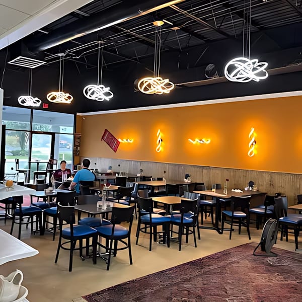 Interior of an Afghan restaurant with modern lighting, orange walls, and blue-seated chairs.
