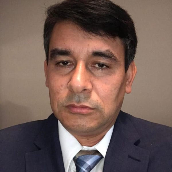 Headshot of a man in a dark suit, white shirt, and blue plaid tie.