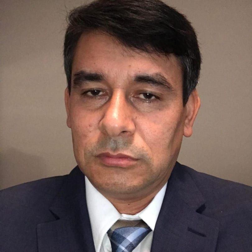Headshot of a man in a dark suit, white shirt, and blue plaid tie.