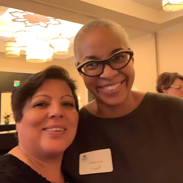 Two smiling women, one with short dark hair and the other with glasses, pose for a selfie.