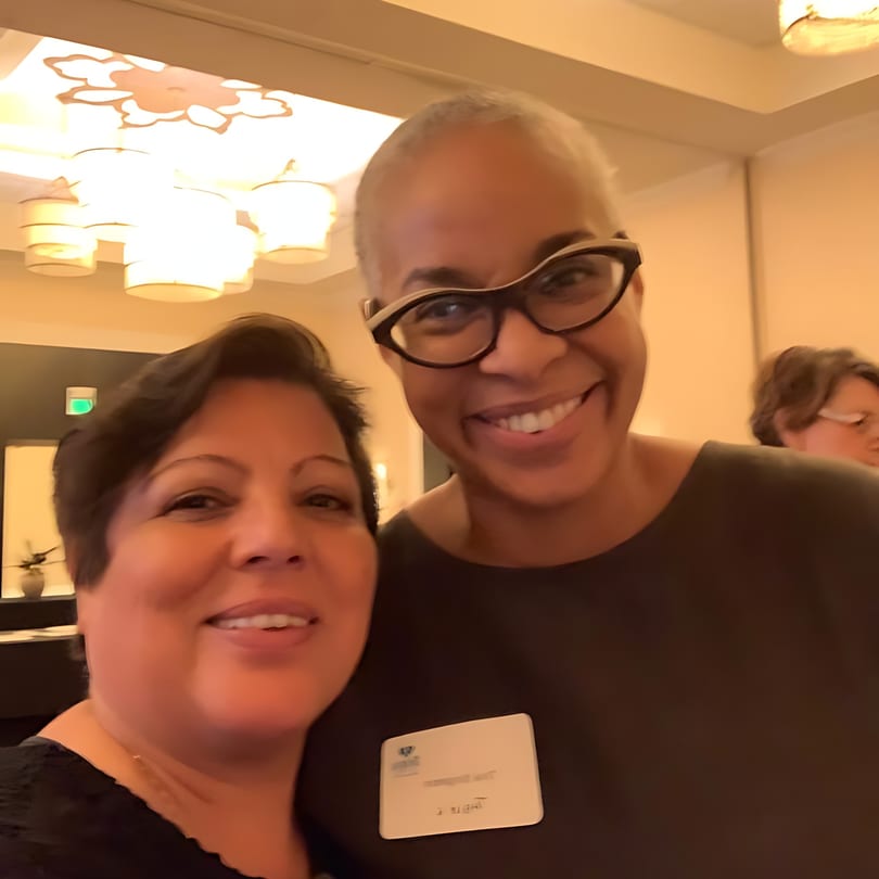 Two smiling women, one with short dark hair and the other with glasses, pose for a selfie.